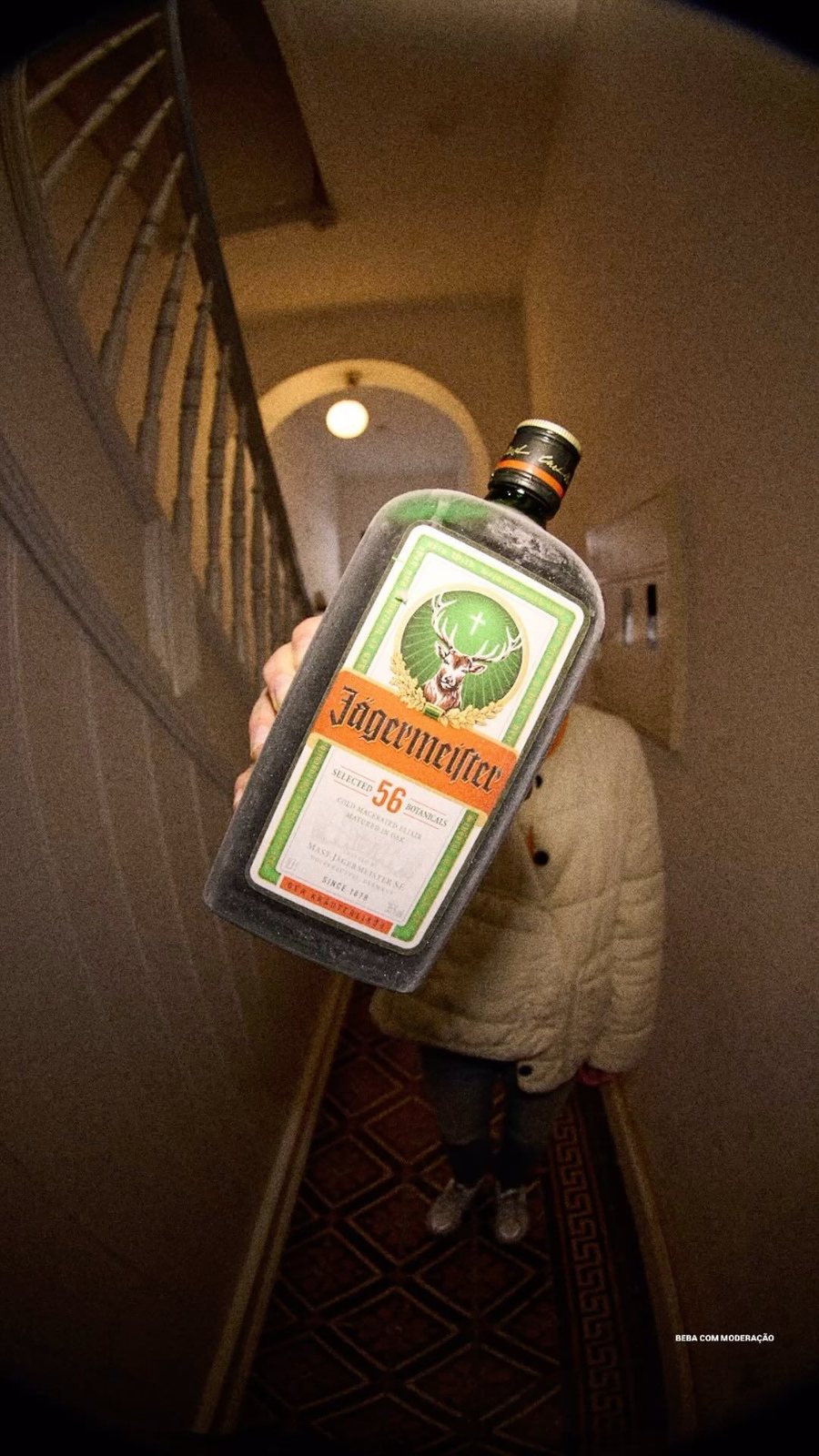 A frosted bottle of Jägermeister held up in a dim stairwell